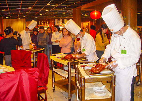 The chef is cutting the roast duck into pieces for the eaters